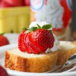 A slice of whipped cream pound cake on a plate topped with strawberries.