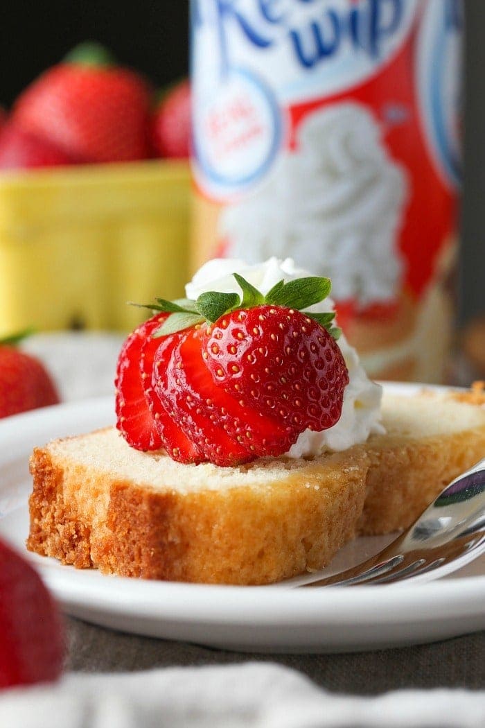 A slice of whipped cream pound cake on a plate topped with strawberries.