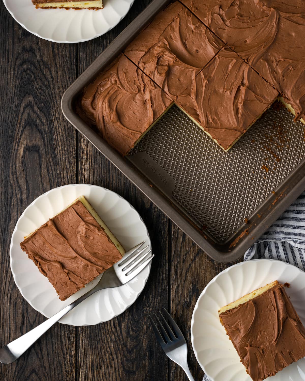 Overhead view of two slices of sour cream cake served on plates, next to the remaining cake in a baking pan.