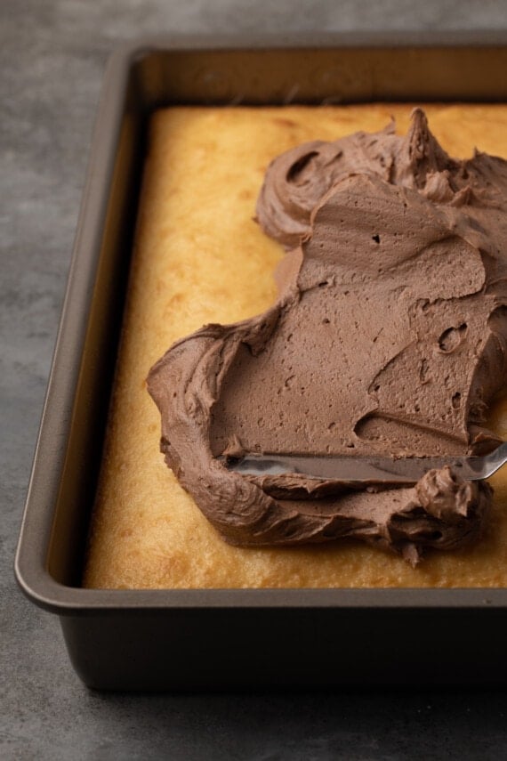 Chocolate frosting is spread over a baked sour cream cake in a cake pan.
