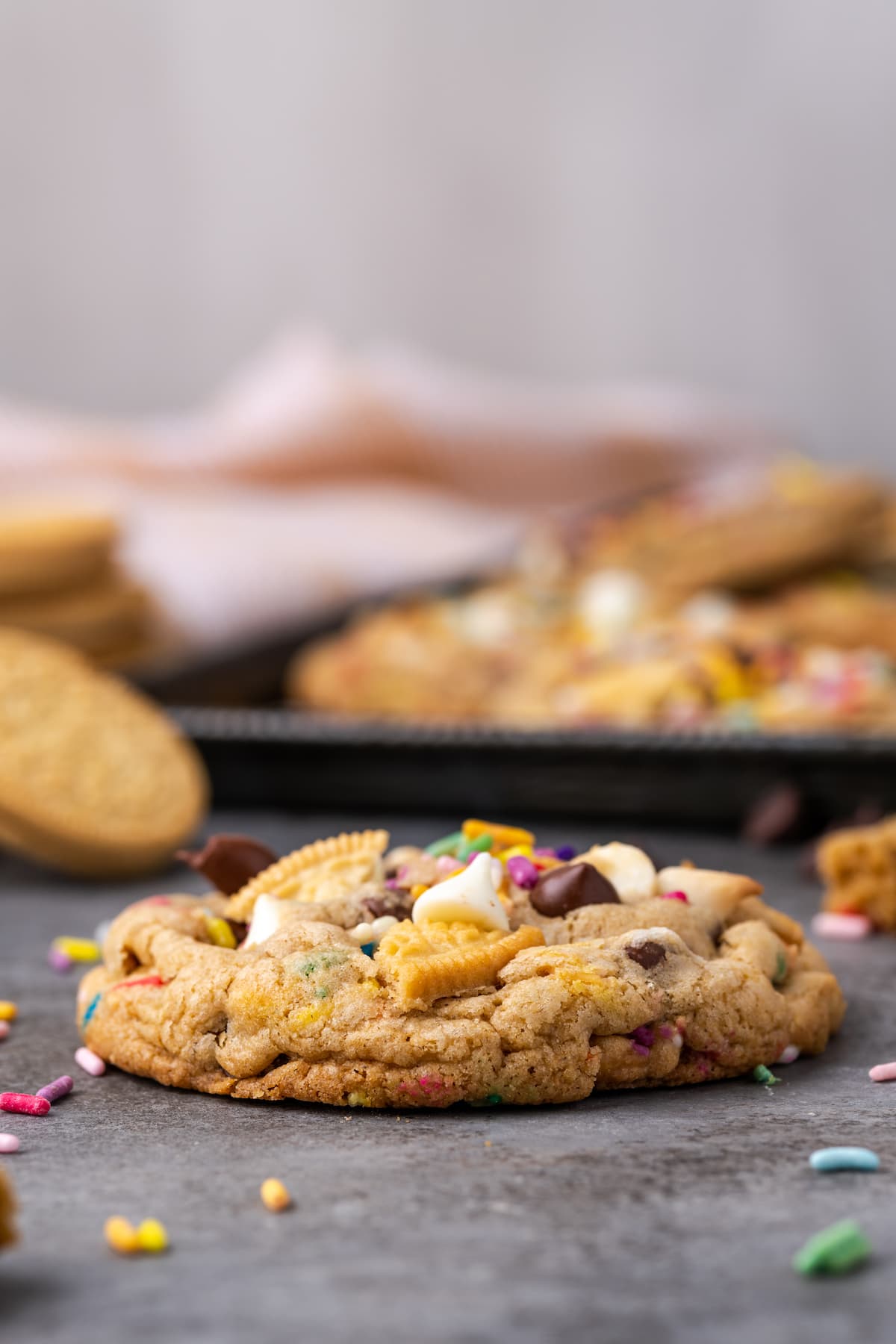 A birthday cake chocolate chip cookie on a countertop with a sheet of cookies in the background.