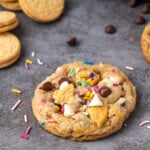 A birthday cake chocolate chip cookie on a countertop, surrounded by more cookies.