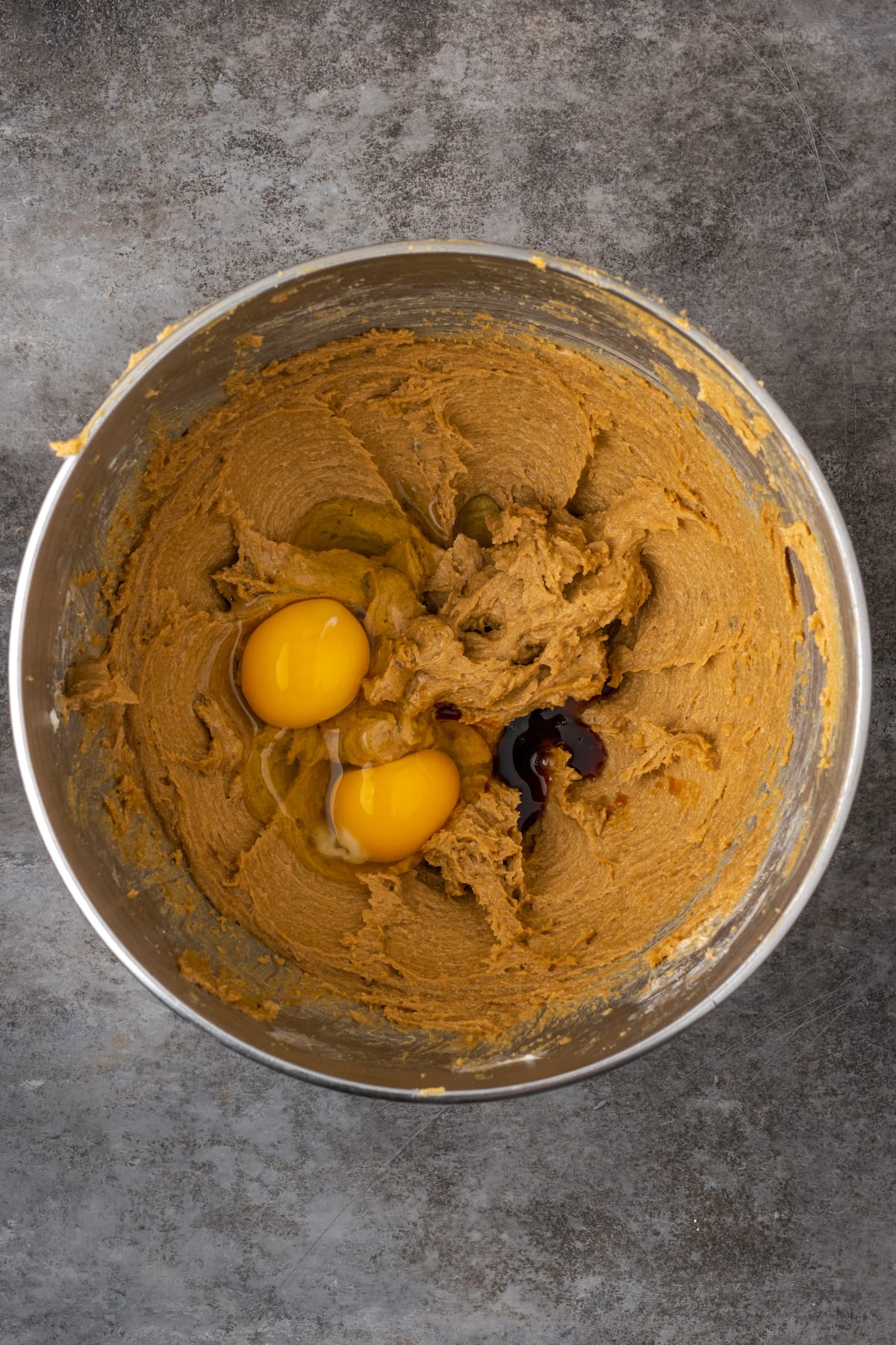 Eggs and vanilla added to the wet ingredients for cookie dough in a metal mixing bowl.