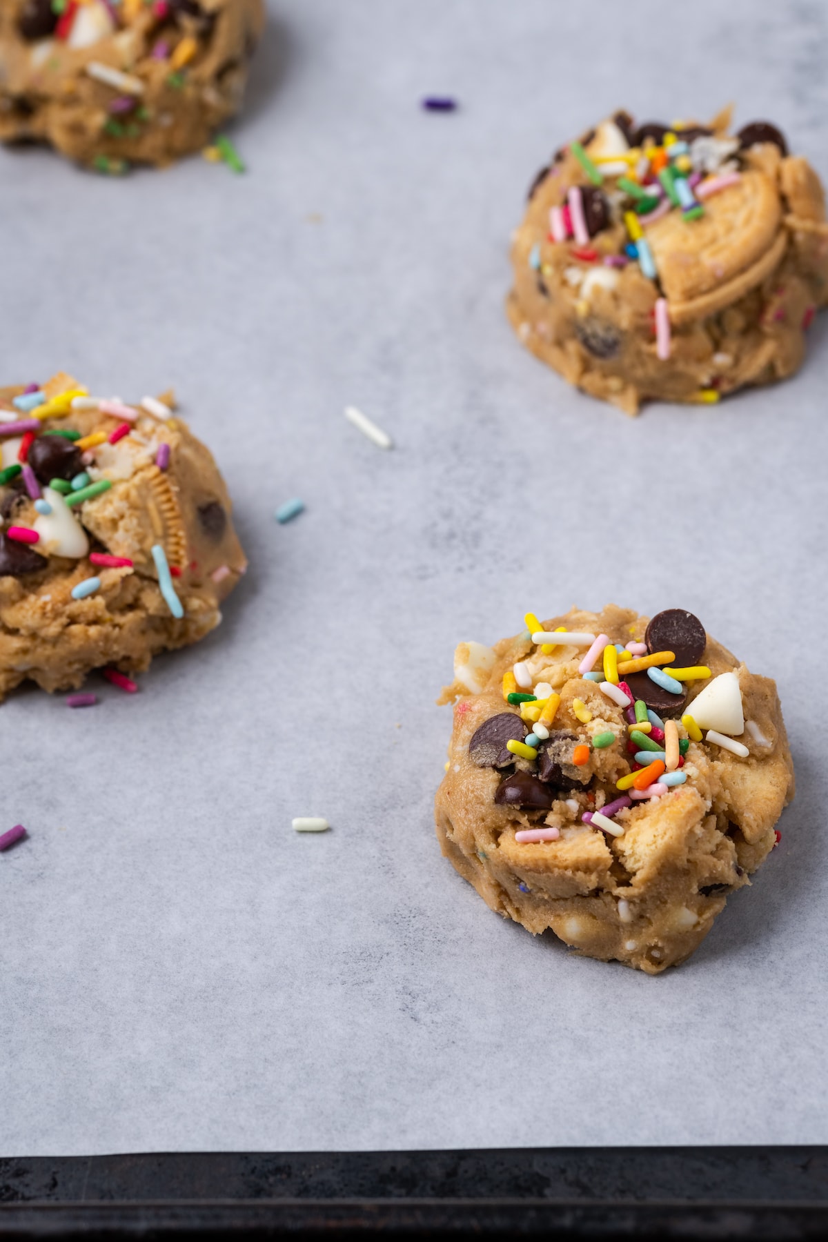 Birthday cake chocolate chip cookie dough portioned out on a lined baking sheet.