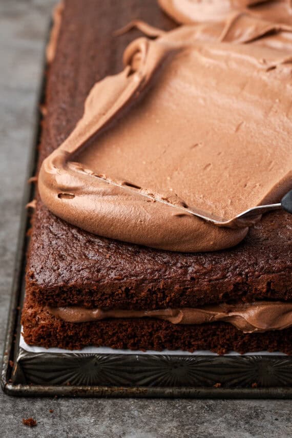 Chocolate frosting partially spread over top of a frosted fudge cake.