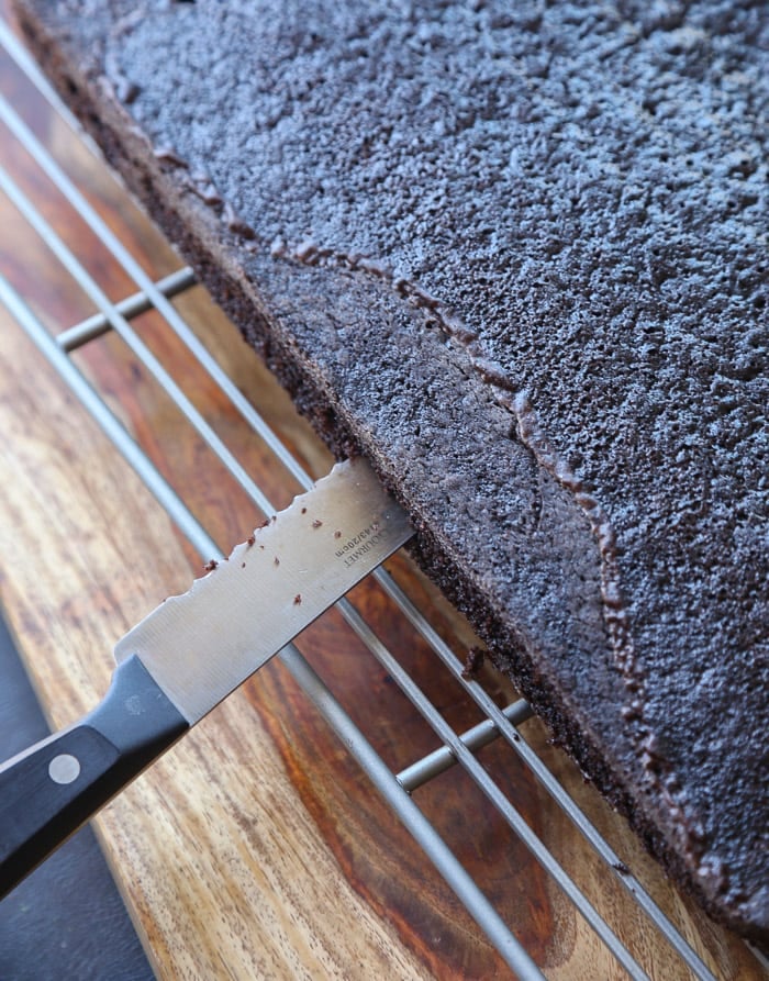 A serrated knife is used to cut the baked chocolate cake into two layers.