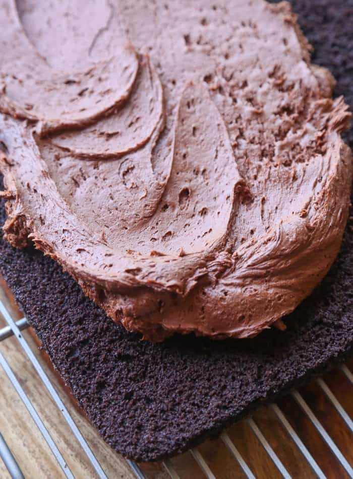 Chocolate frosting is spread overtop of a layered fudge cake.