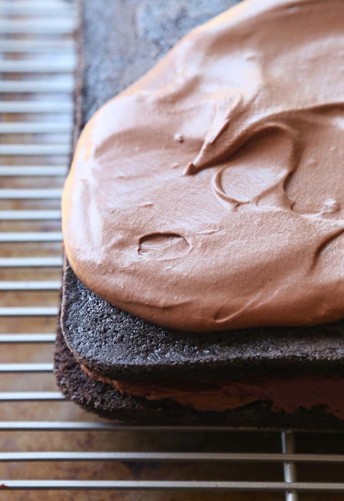 Chocolate frosting is spread overtop of a layered chocolate cake.