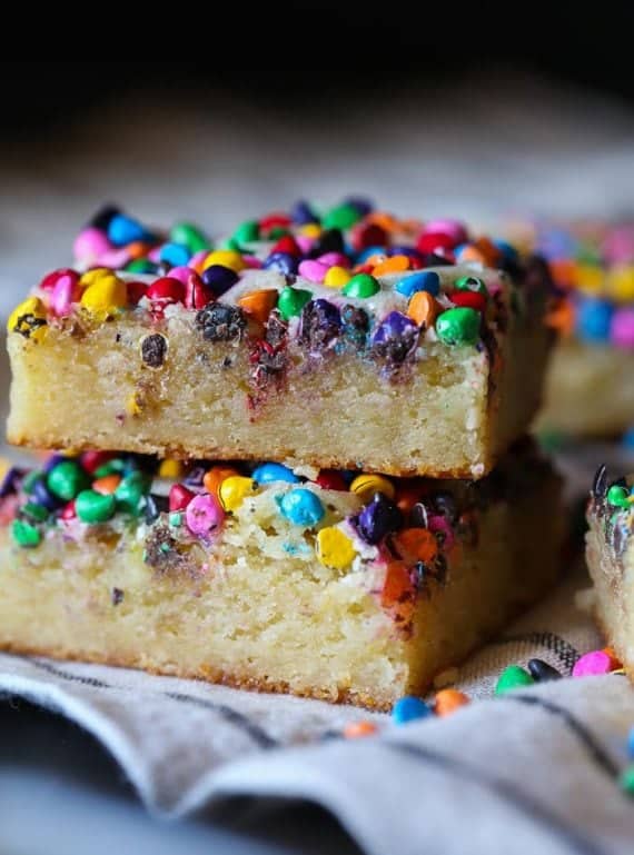 Rainbow chip white chocolate blondies stacked on a kitchen towel.