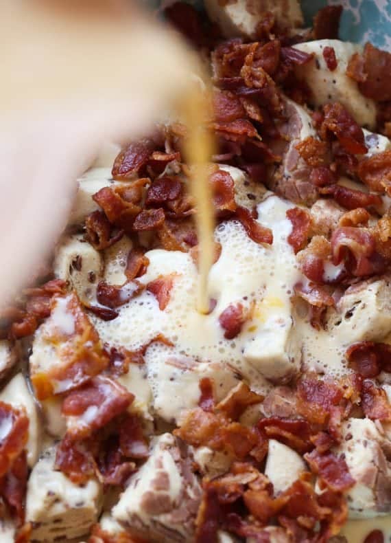 Egg mixture being added to Cinnamon Roll chunks and bacon in a baking dish