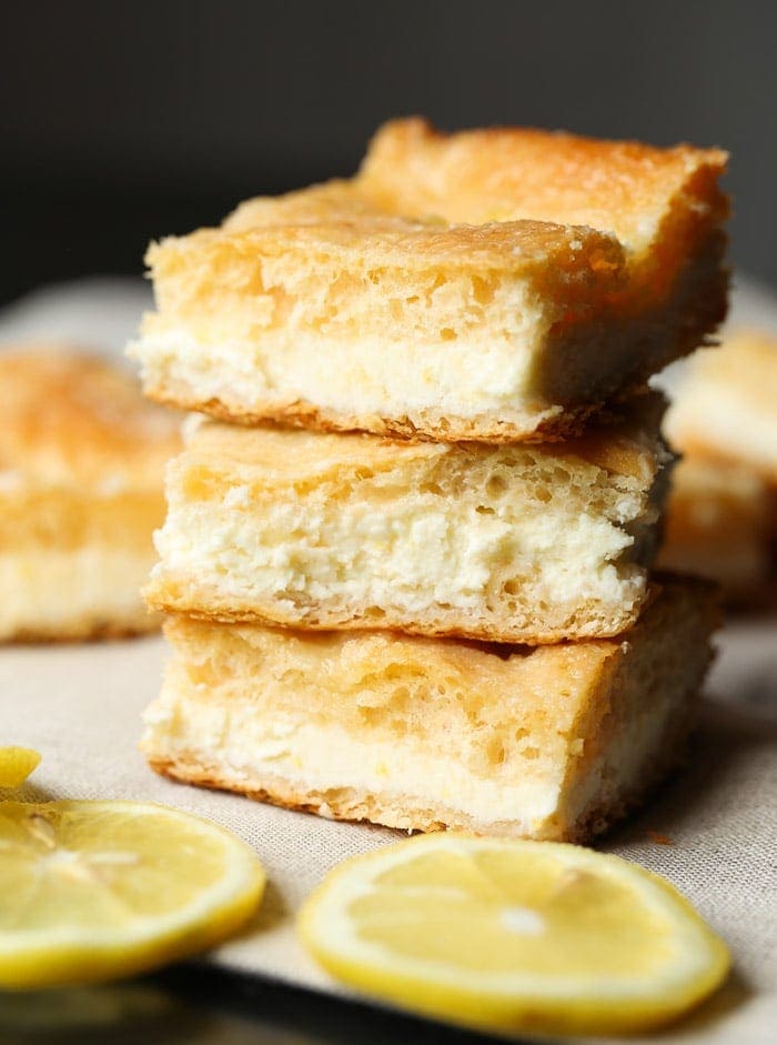 A stack of three lemon cream cheese bars surrounded by lemon wedges.