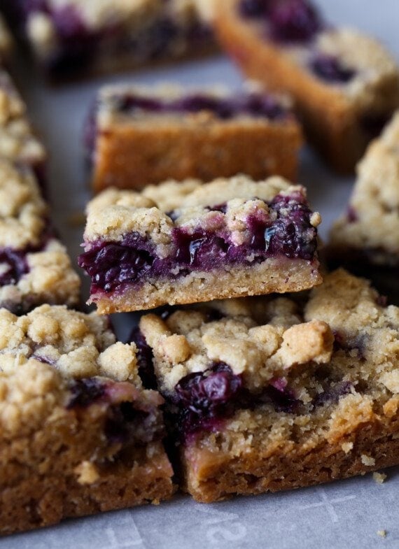 Bars with a shortbread crust, blueberry filling, and crumb topping cut and stacked showing the filling