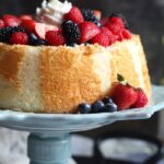 Angel Food Cake topped with mixed wine-soaked berries on a blue cake stand.
