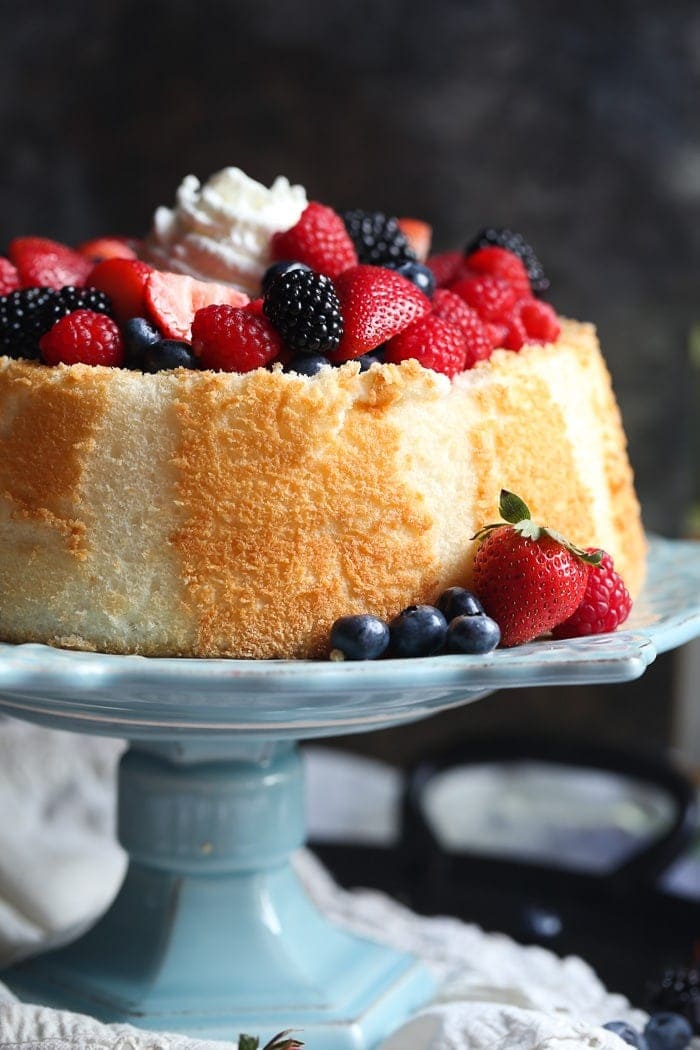 Angel Food Cake topped with mixed wine-soaked berries on a blue cake stand.