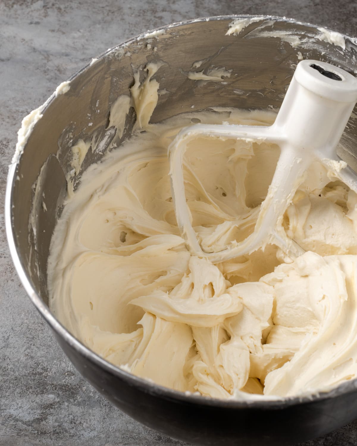 Cream cheese frosting in a metal bowl with the head of a stand mixer.