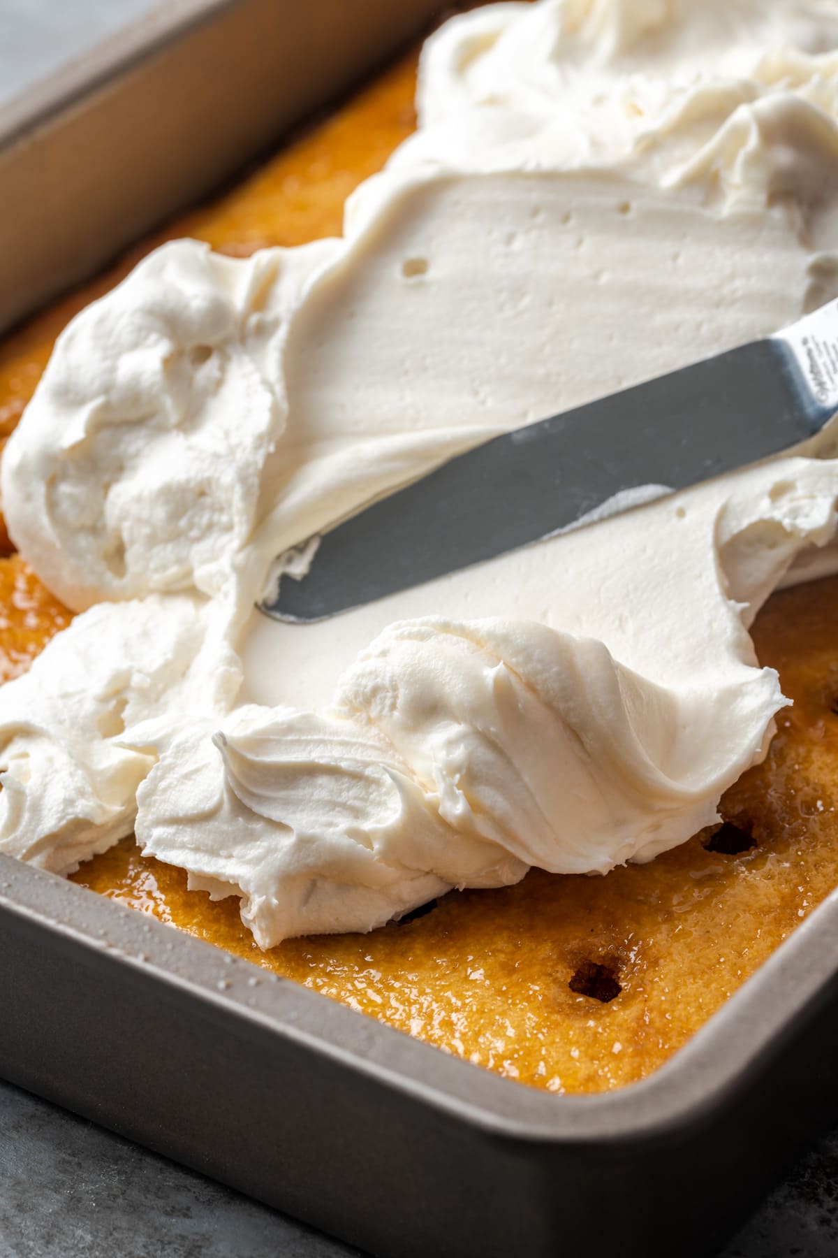 An offset spatula is used to spread cream cheese frosting over a cake soaked with caramel.
