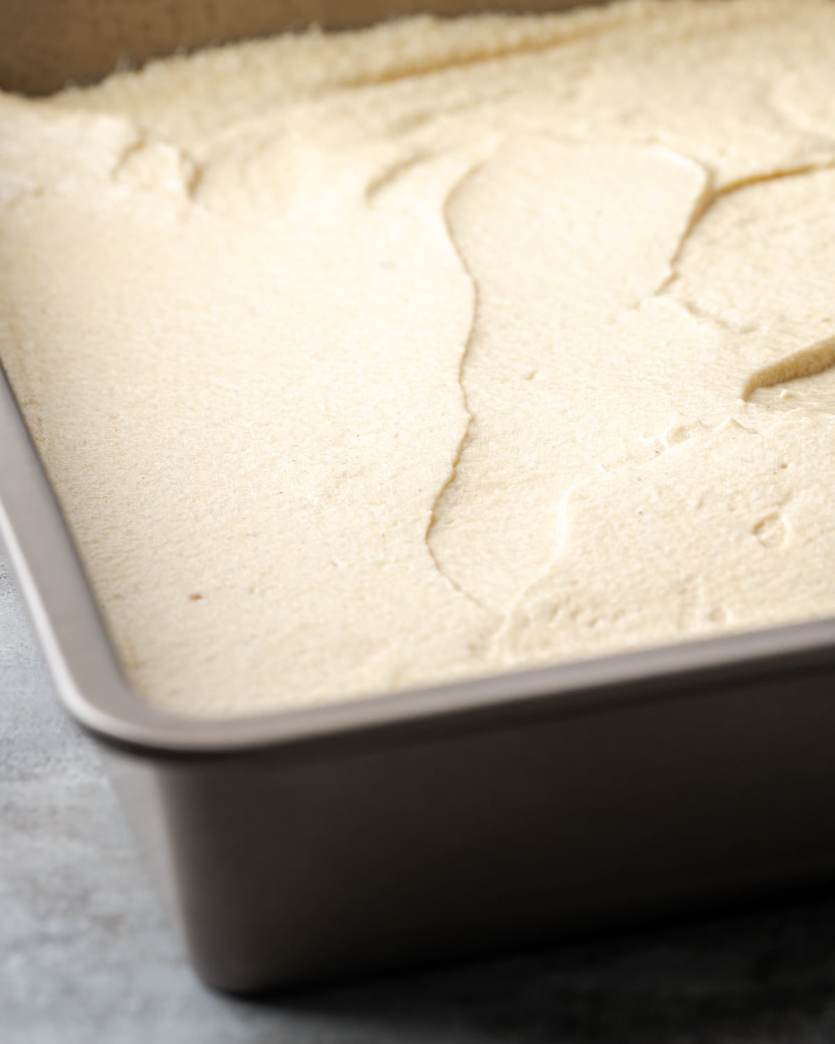 Vanilla cake batter spread evenly in a metal baking pan.