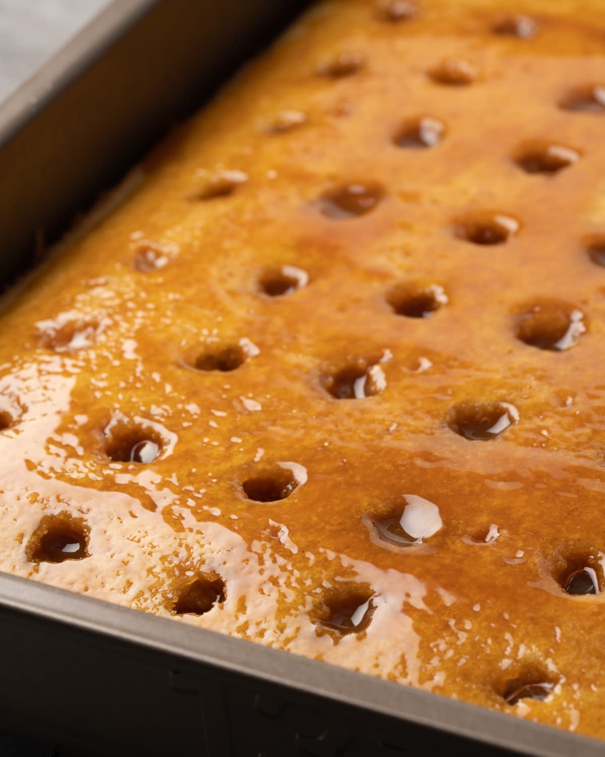 Vanilla cake in a pan, with holes poked in the surface, covered in a layer of caramel sauce.