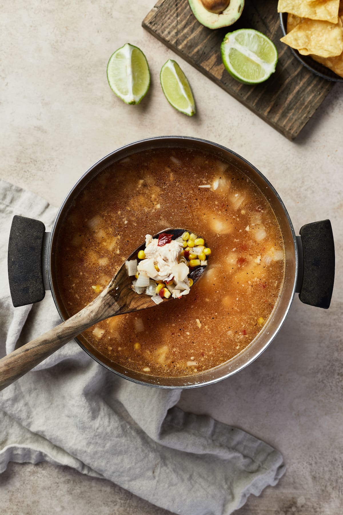 A wooden spoon lifts the ingredients from a pot of Mexican chicken soup.