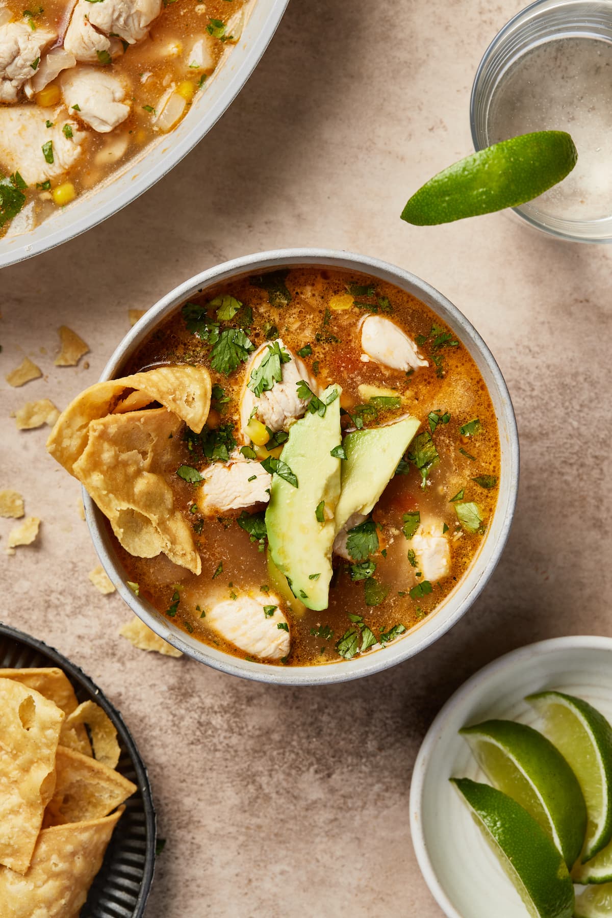 A bowl of Mexican chipotle lime chicken soup garnished with tortilla chips and avocado.