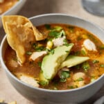 A bowl of Mexican chipotle lime chicken soup garnished with tortilla chips and avocado.