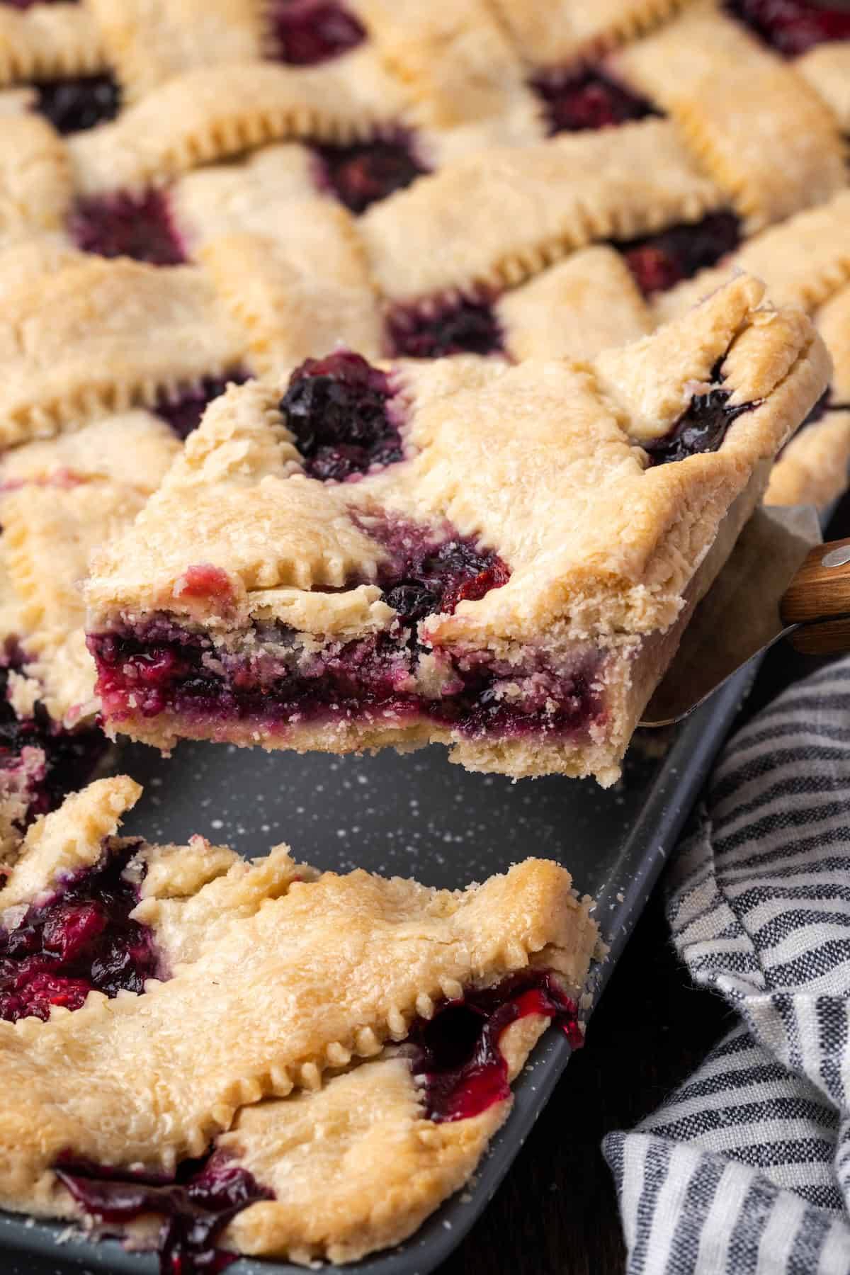 A slice of berry slab pie being lifted from the pan with a spatula.