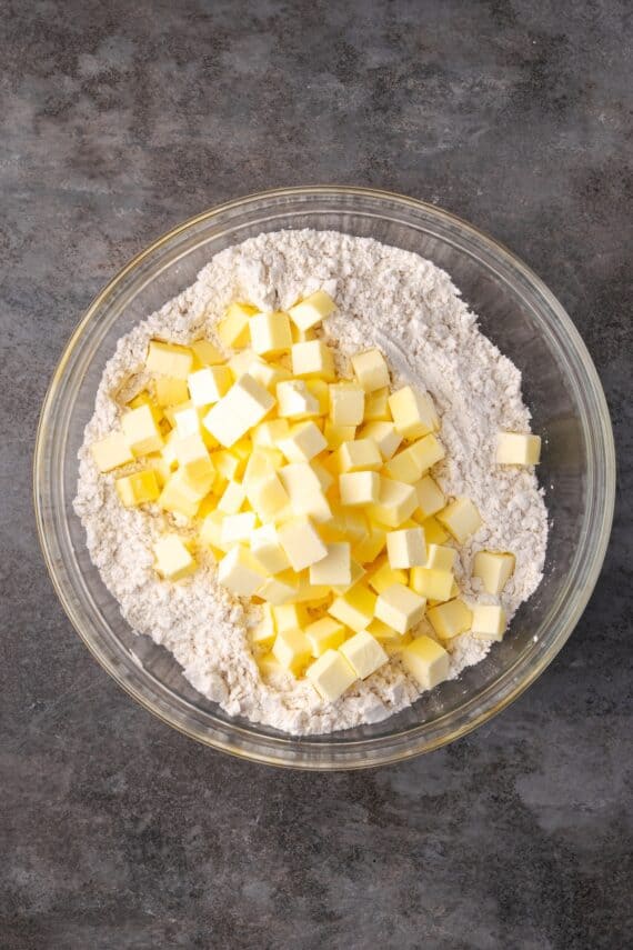 Cubed butter added to dry pie dough ingredients in a bowl.