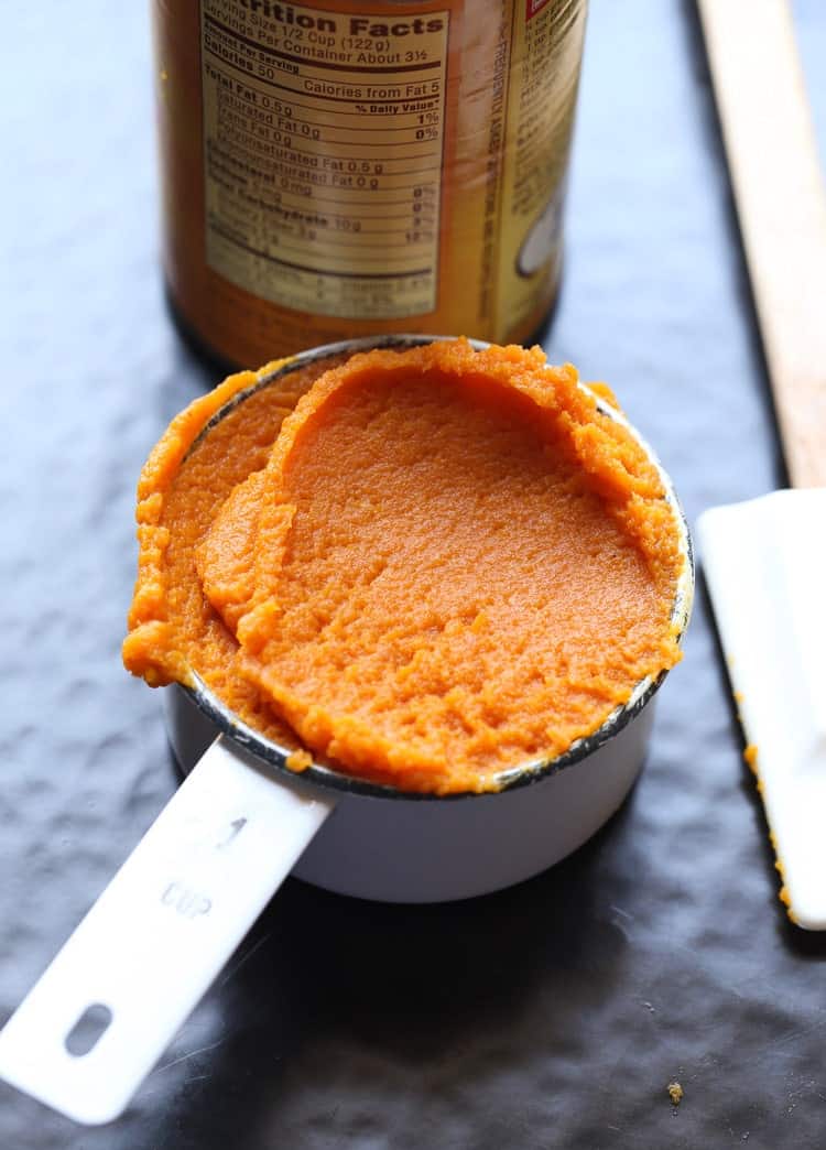 A measuring cup full of pumpkin puree next to a can of it.