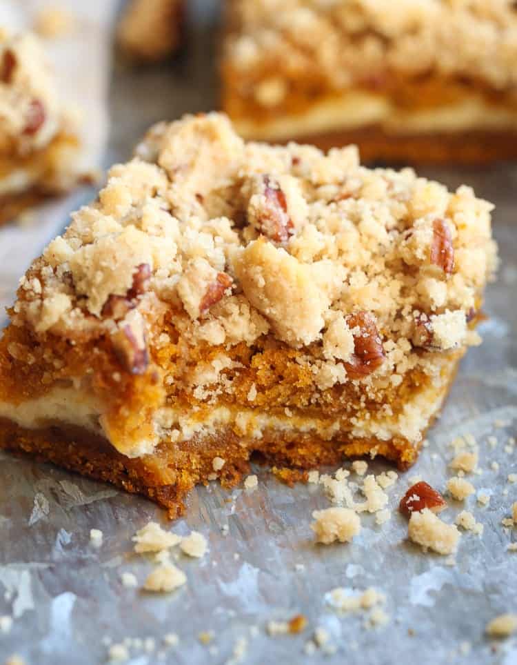 A pumpkin square filled with cream cheese and topped with praline on a countertop, with a bite missing