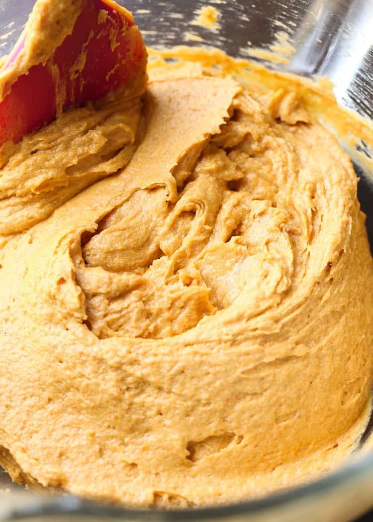 Close up of pumpkin cake batter in a bowl with a rubber spatula. 