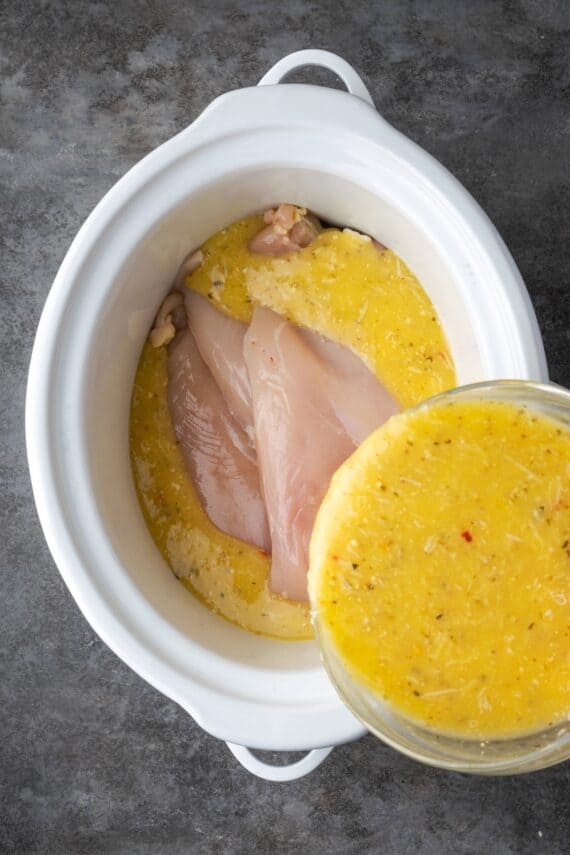 Italian parmesan dressing being poured over chicken breasts inside the crock pot.