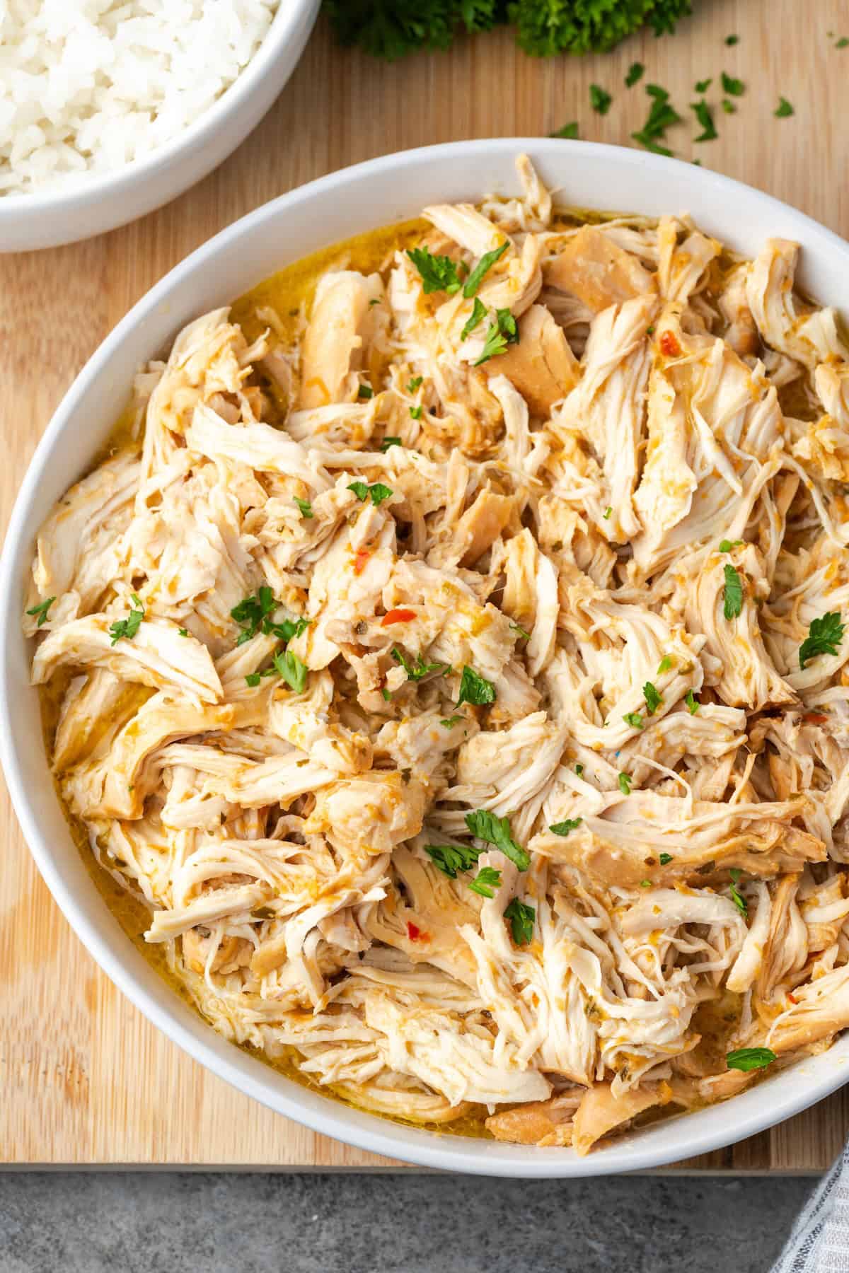 Elevated landscape of Italian chicken in a slow cooker chopped in a large white bowl.