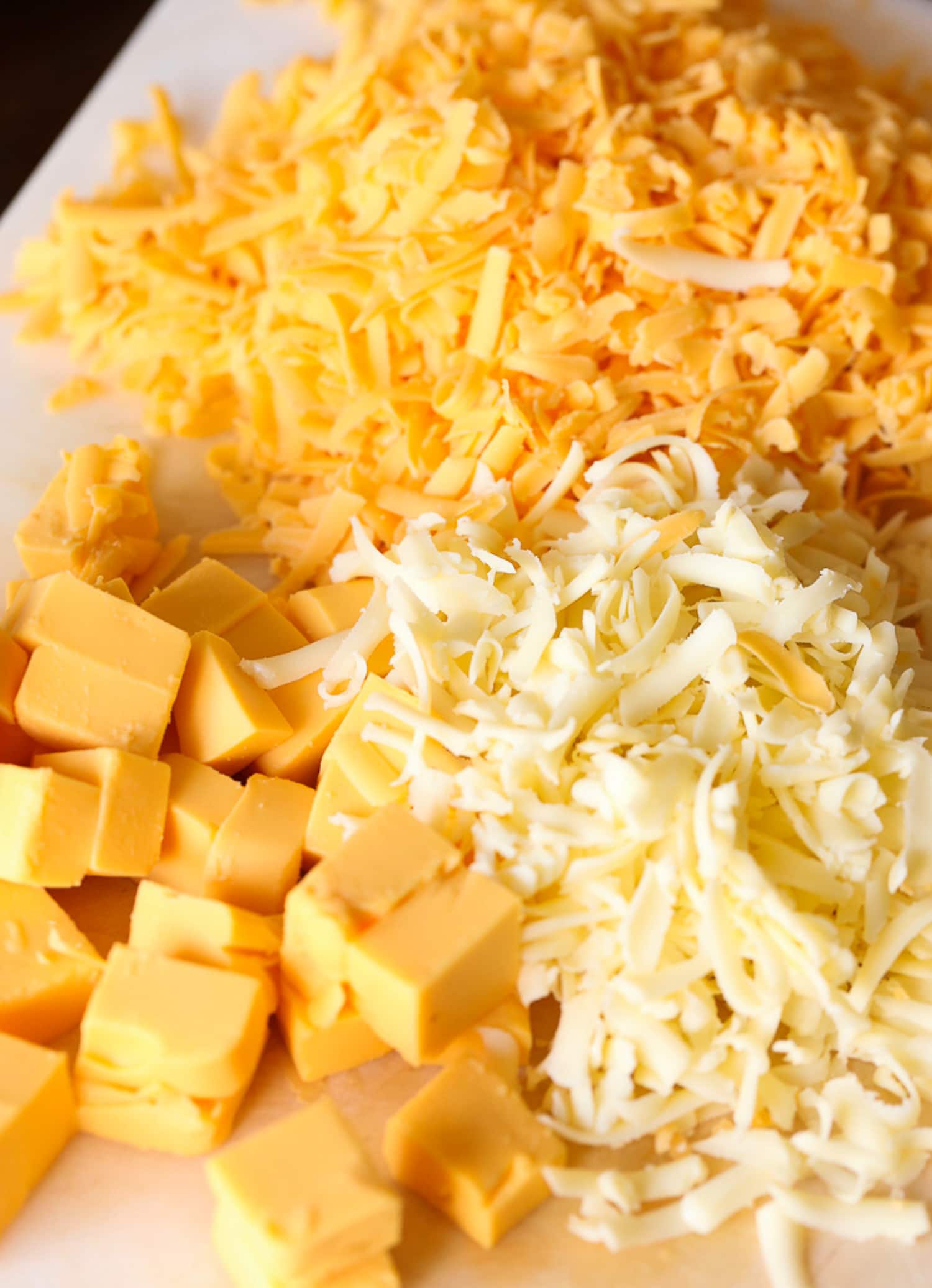 three types of cheese grated on a cutting board