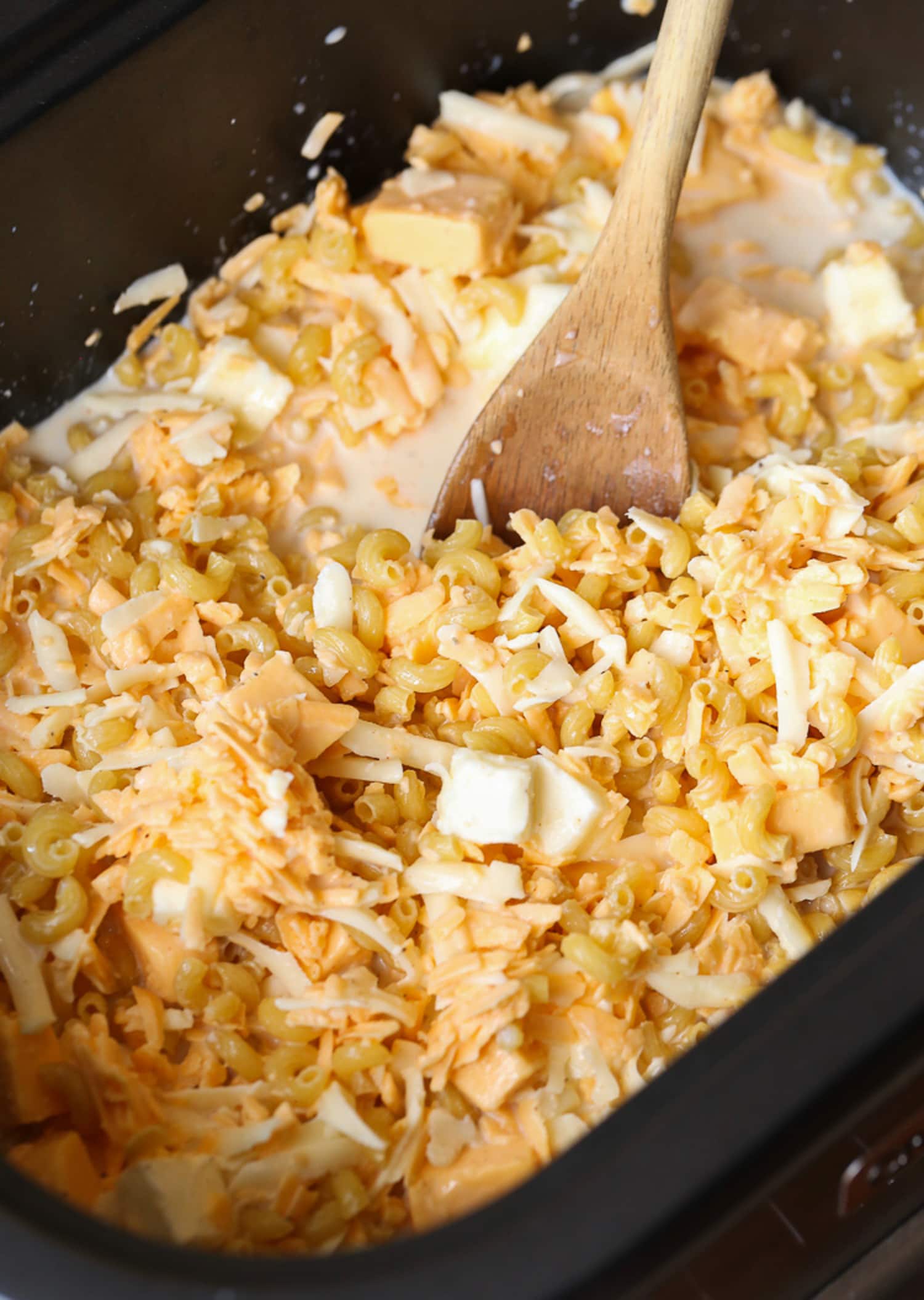 mixing pasta, milk and grated cheeses in a slow cooker with a wooden spoon