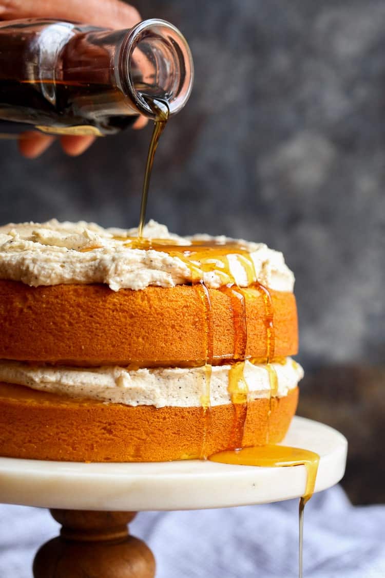 Syrup is poured over a Perfect Pumpkin Cake with Maple Frosting.