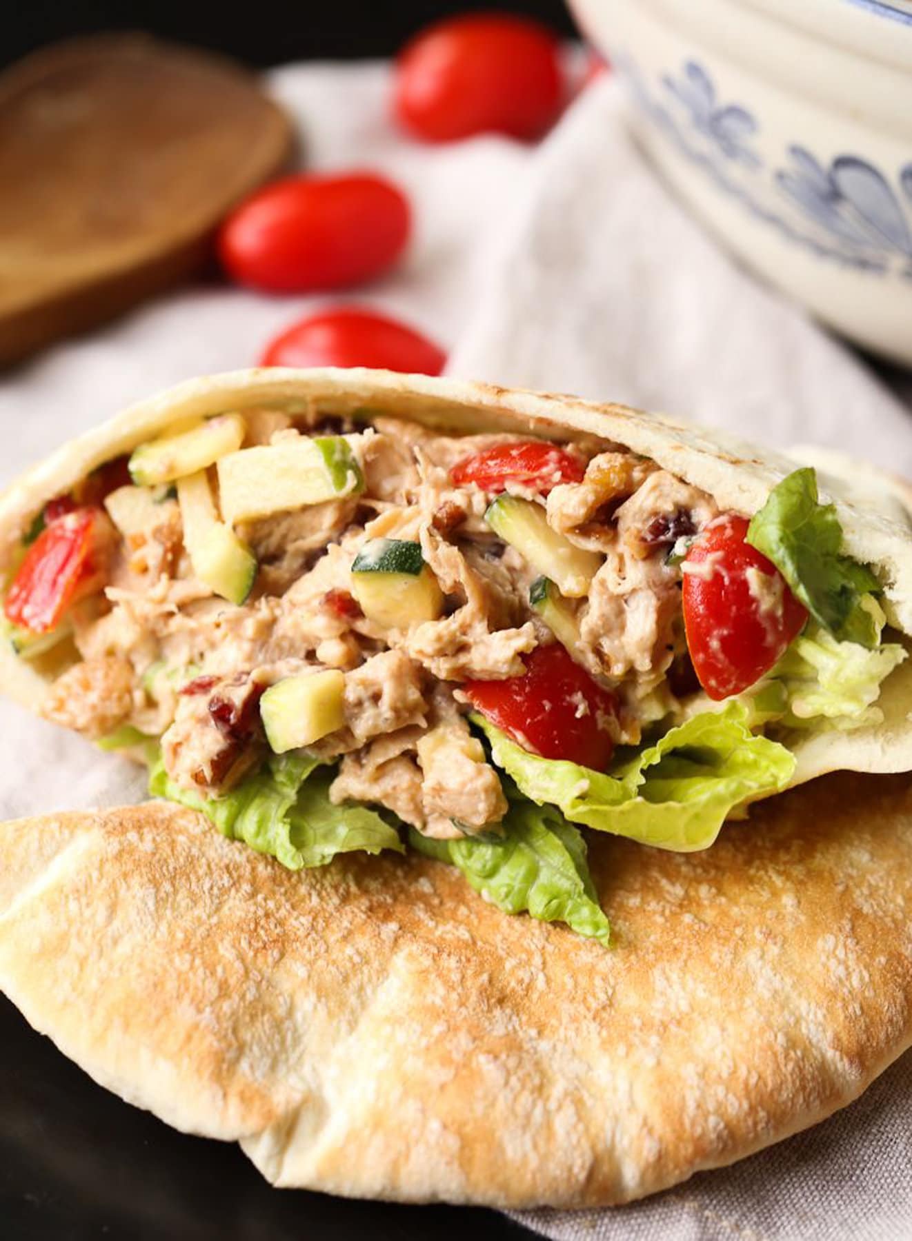 A crunchy chicken salad inside of a piece of pita bread on a table with cherry tomatoes