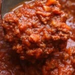 Close up of a spoon scooping bolognese sauce from the slow cooker.