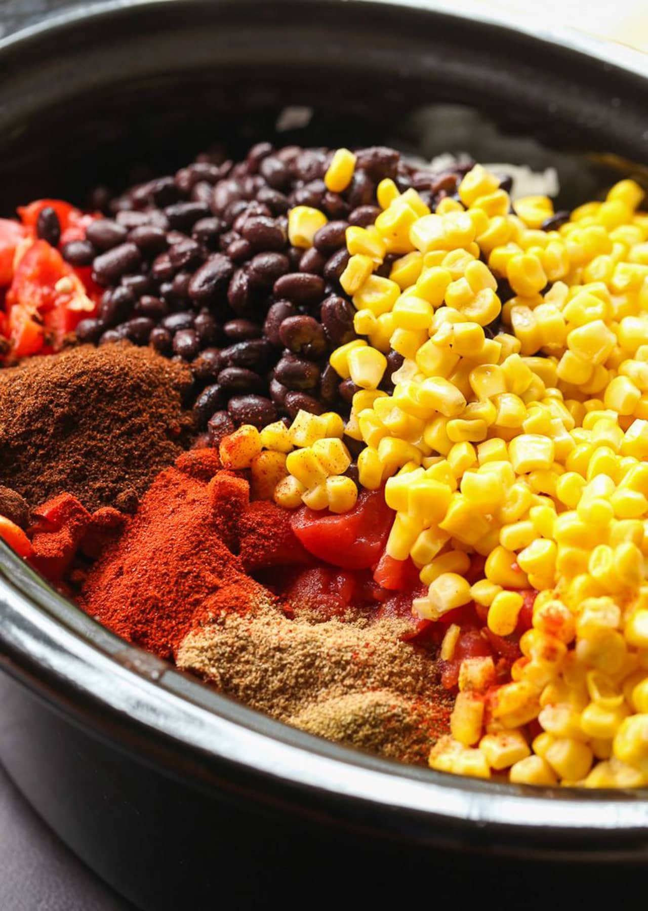 The ingredients for taco truck chili in the bowl of a slow cooker: beans, corn, tomatoes and diced green chilies, herbs, and spices.