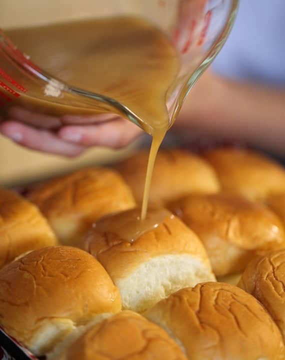Melted butter and maple syrup being poured over Maple Sausage Breakfast Sliders in a pan