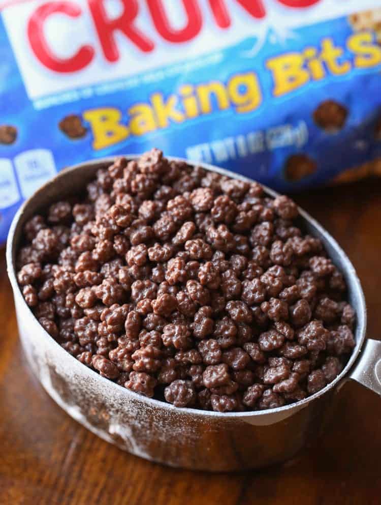 Nestle Crunch Baking Bits in a Metal Measuring Cup on a Wooden Table