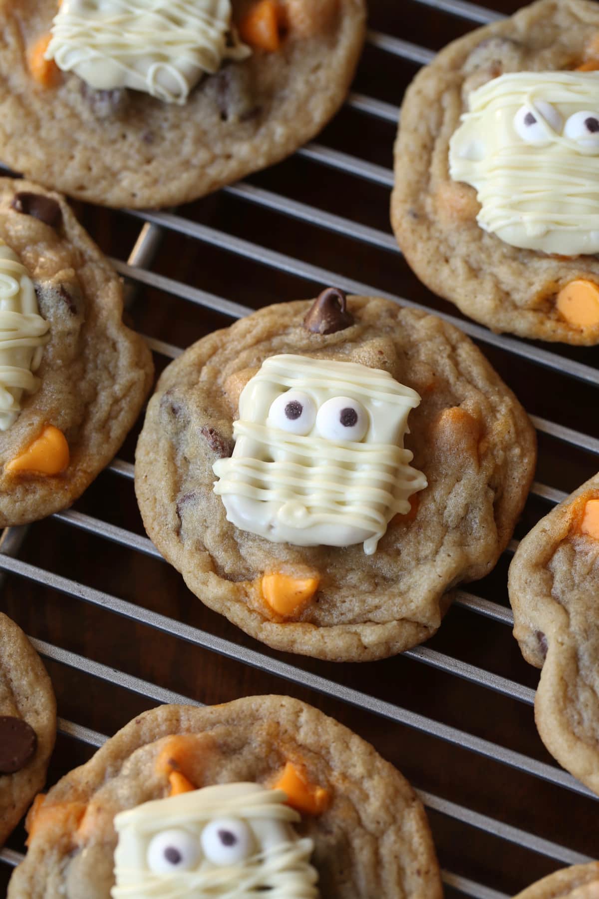 A white chocolate covered pretzel decorated like a mummy on top of a chocolate chip cookie