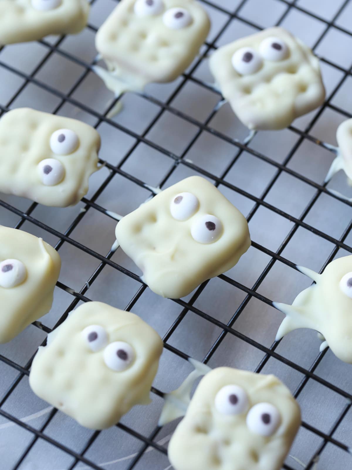 Waffle pretzels covered in white chocolate with 2 candy eyes on a wire rack