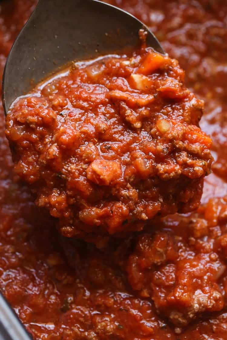 A spoon lifts slow cooker bolognese sauce from a pot.