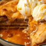 A skillet apple pie topped with scoops of vanilla ice cream with a large slice missing.