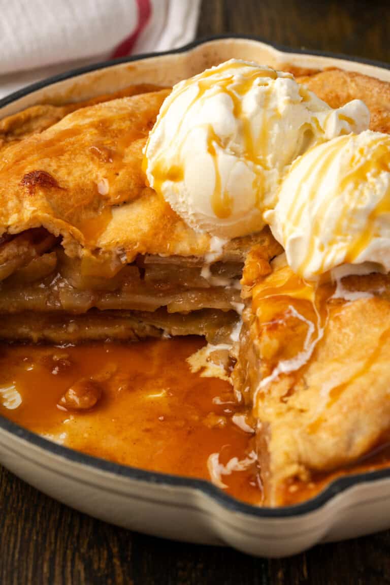 A skillet apple pie topped with a scoop of vanilla ice cream is missing a large slice.