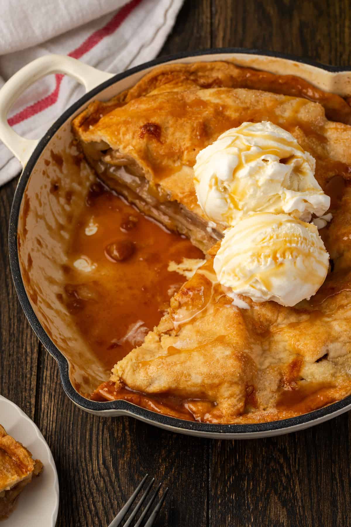 A skillet apple pie topped with scoops of vanilla ice cream with a large slice missing.