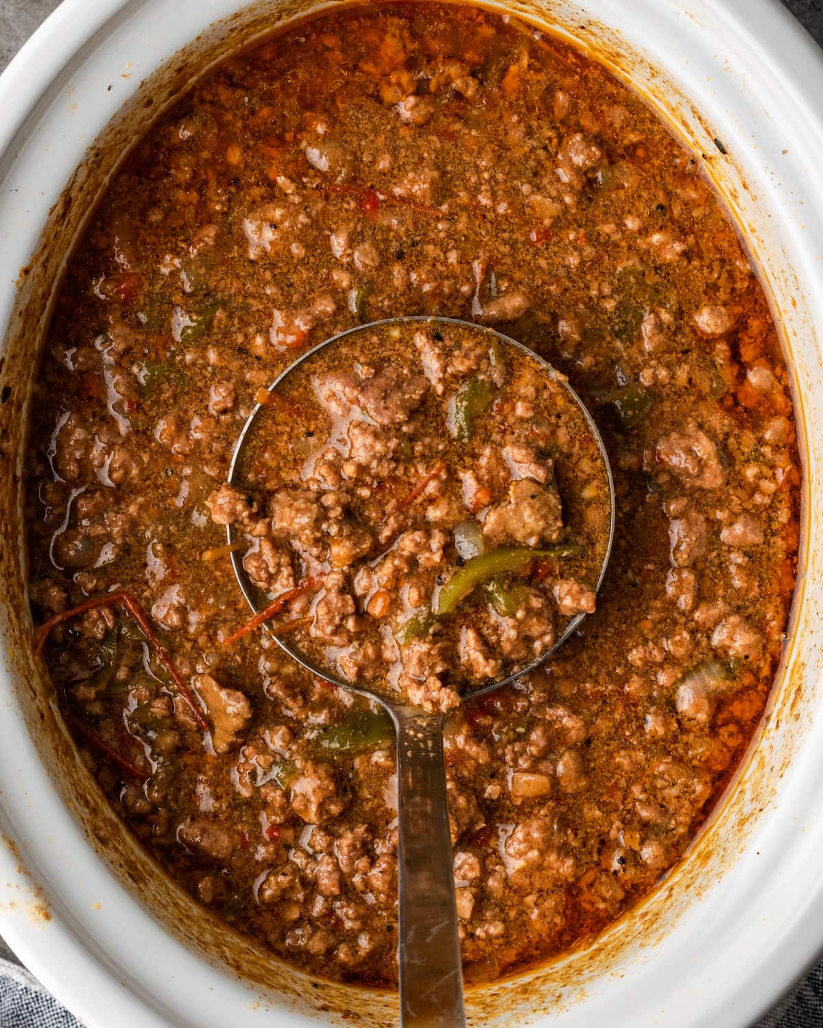 Overhead view of Philly Cheesesteak Sloppy Joes in a crock pot with a ladle.
