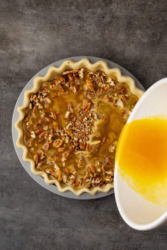 Syrup topping being poured over the assembled cheesecake pecan pie.