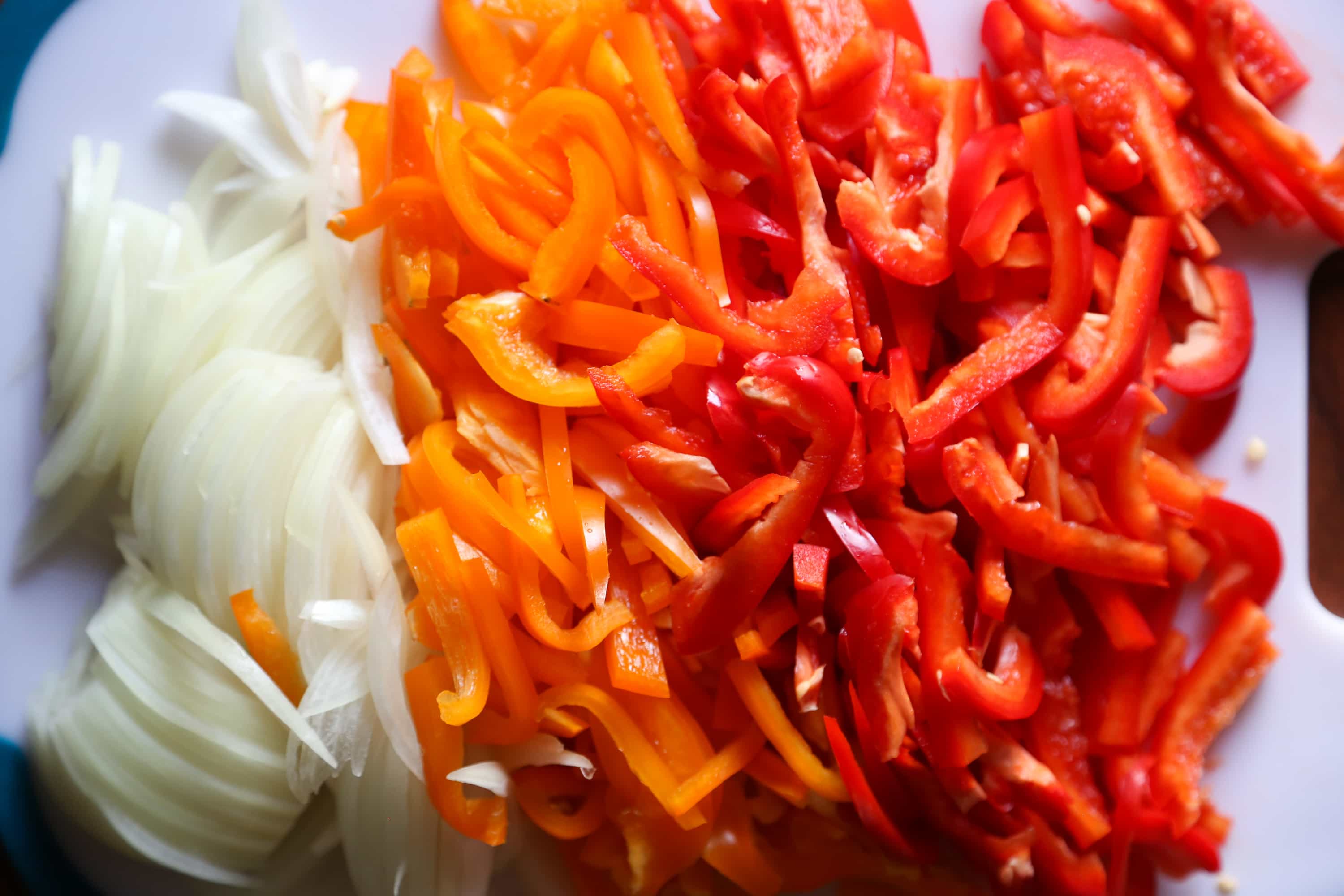 Chopped red bell peppers, orange bell peppers and onions on a plastic cutting board