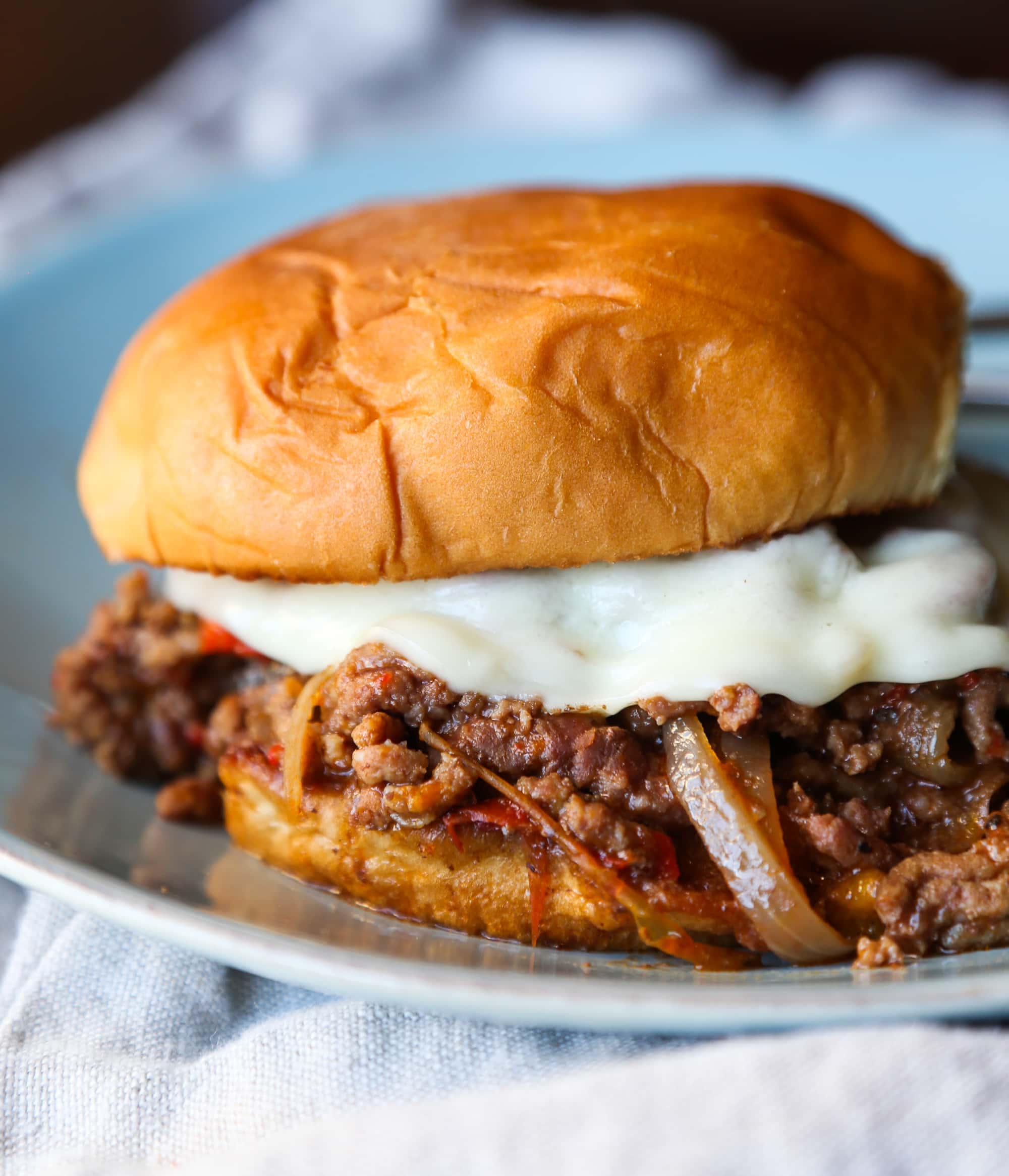 A crock pot philly cheesesteak sloppy joe on a white plate over a kitchen towel